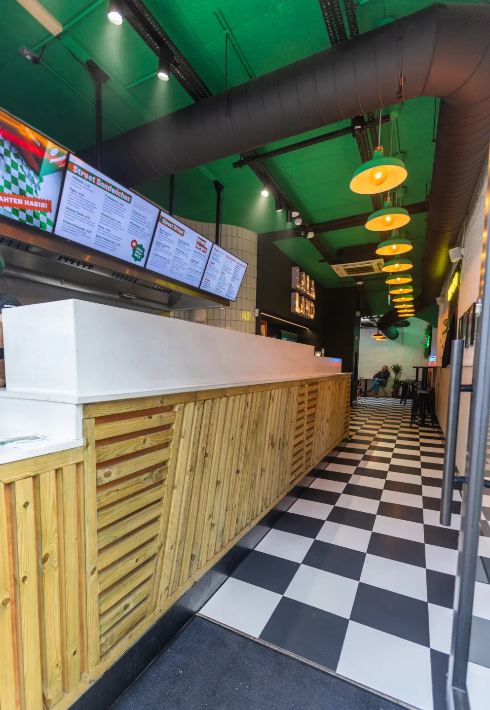 Full-length timber-clad service counter beneath digital menu boards — Mayyil, Notting Hill