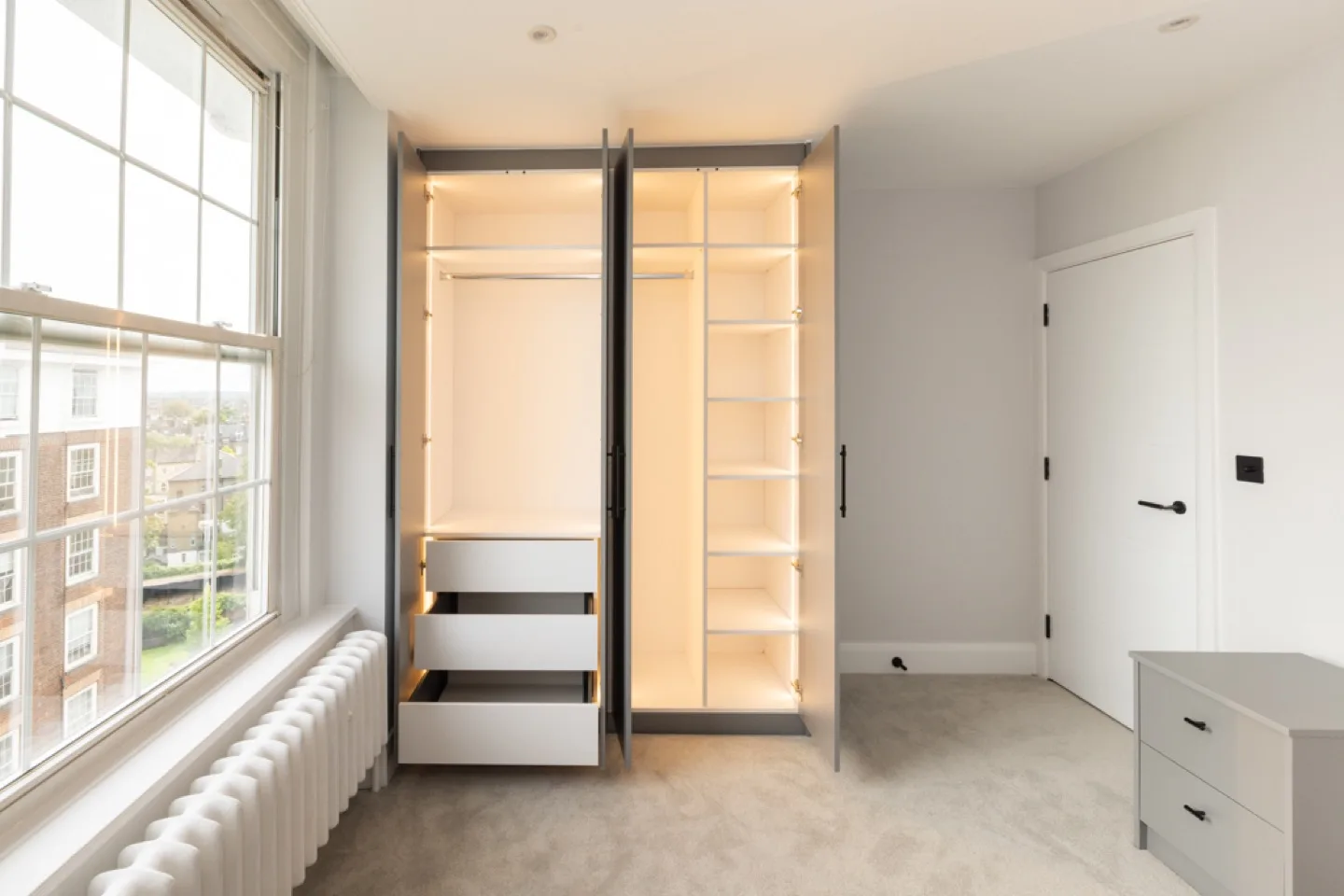 Open grey wardrobe showing LED-lit white interior with hanging rail, drawers and adjustable shelving