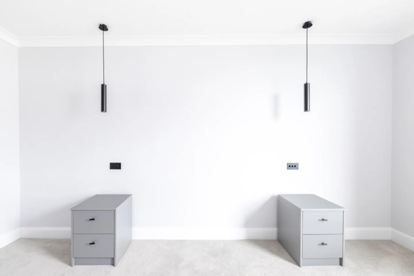 Pair of matching grey two-drawer bedside tables with black handles beneath pendant lights