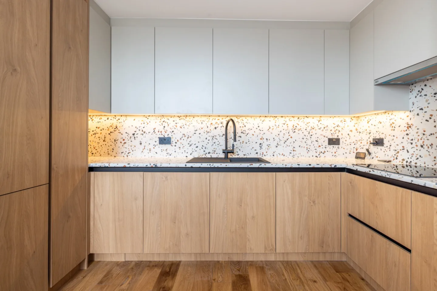 Two-tone oak and off-white U-shaped kitchen with terrazzo splashback and black tap and sink