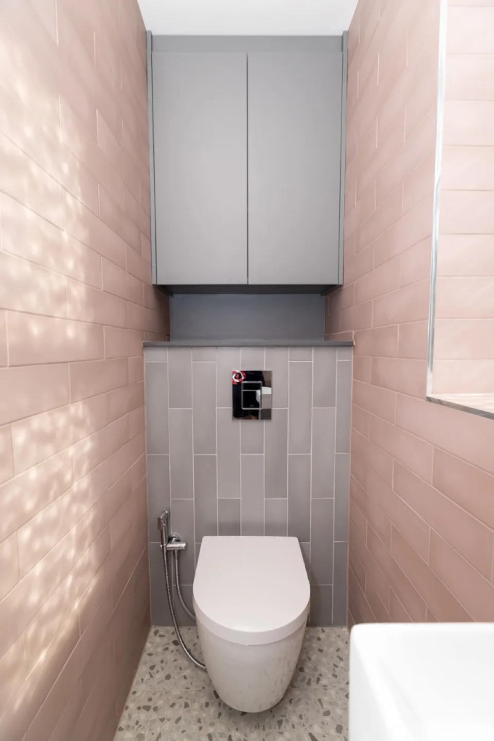 Grey wall cabinet fitted above the WC in a pink-tiled bathroom with terrazzo flooring