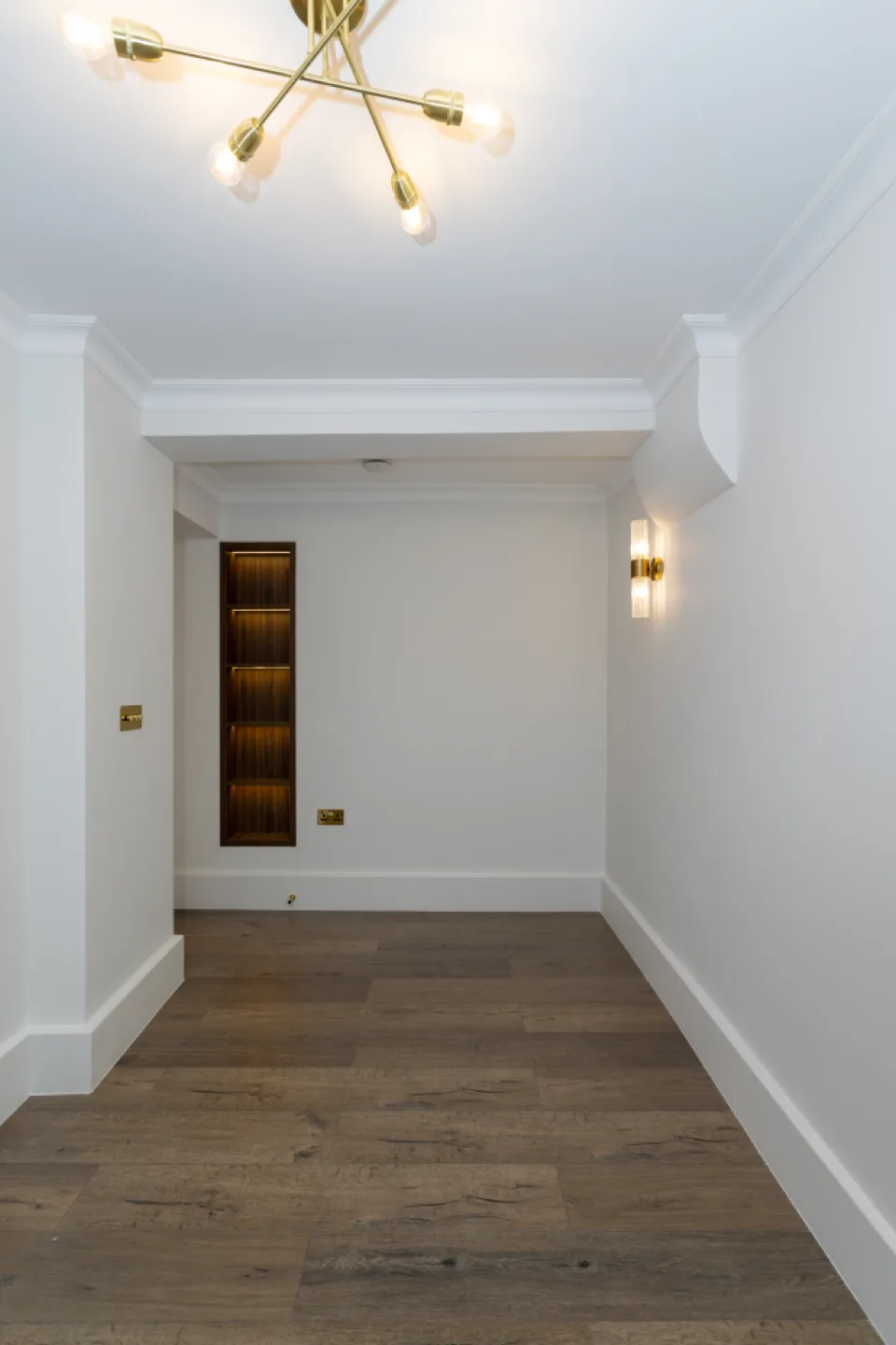 Built-in recessed walnut display unit with LED-lit shelves set into a bedroom wall above oak flooring