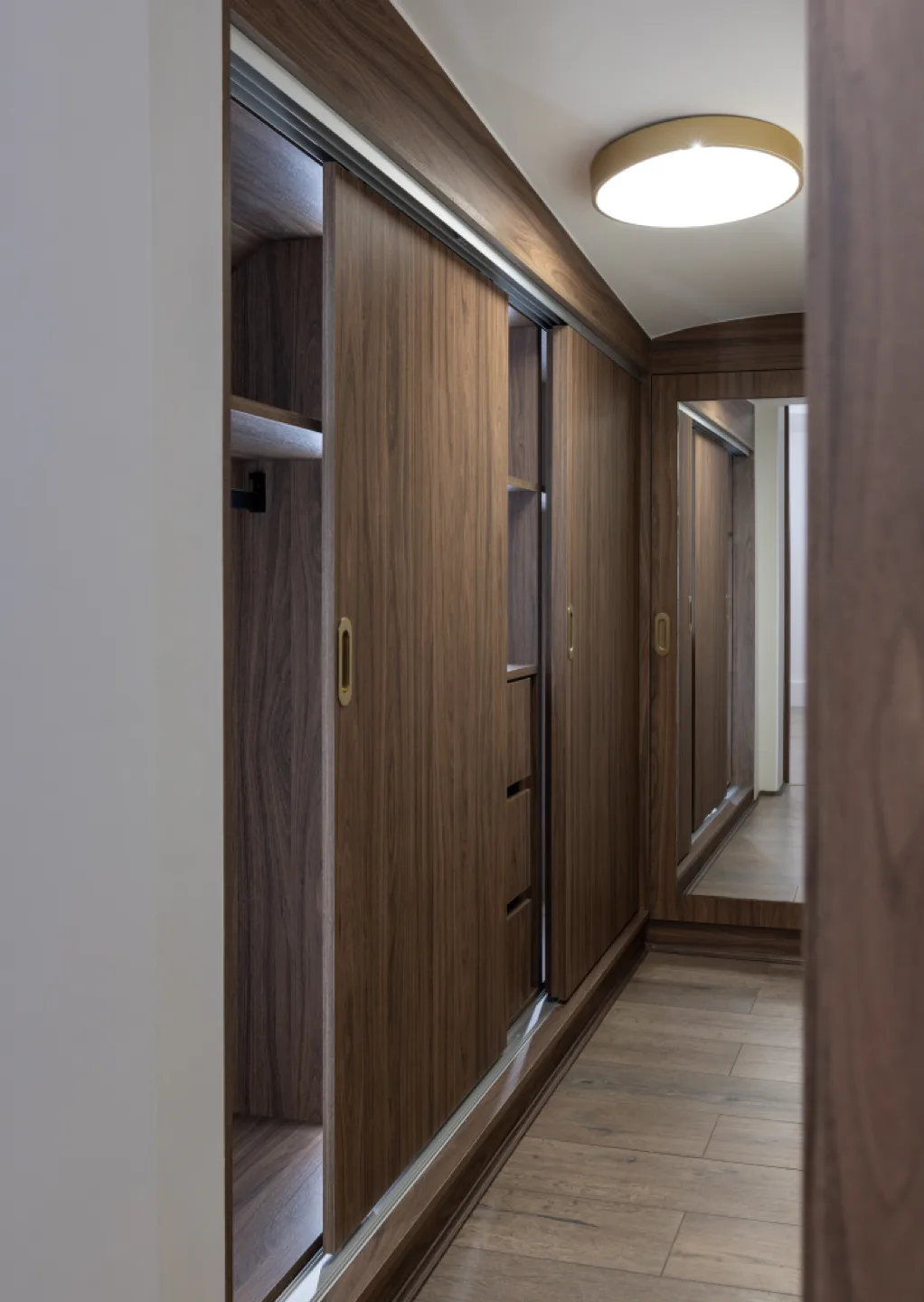 Walk-in wardrobe with walnut sliding doors, brass recessed handles and internal rails, drawers and shelving