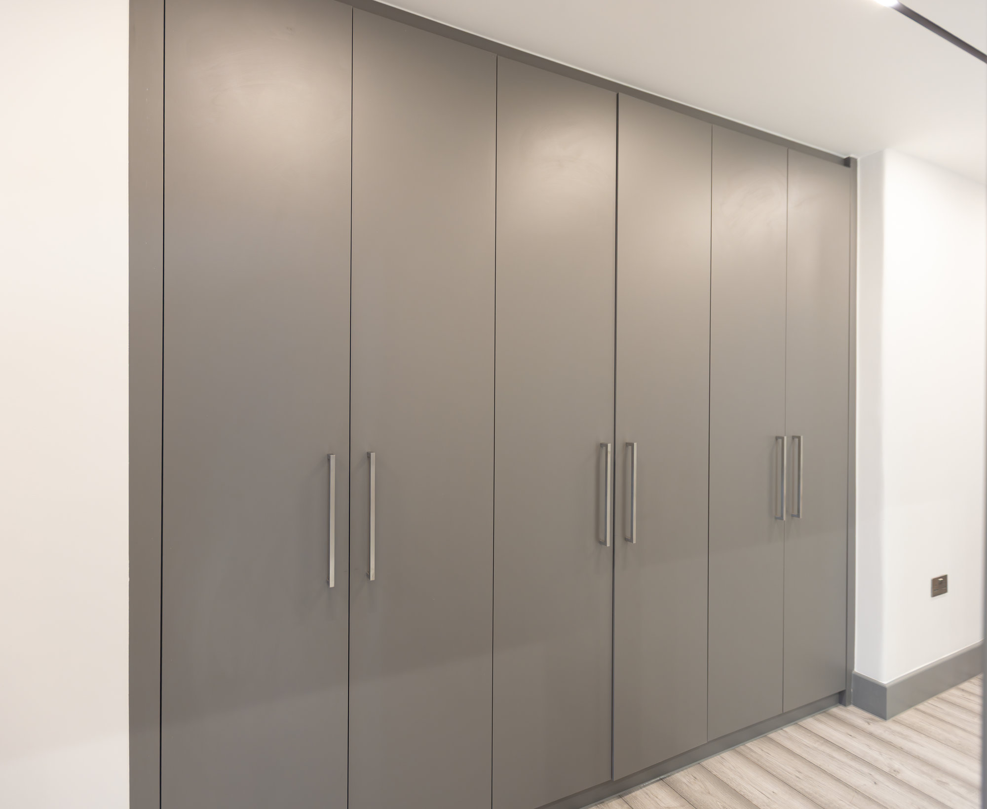 Bespoke fitted wardrobe with smooth grey doors and brushed chrome bar handles spanning the full wall in a Kensington hallway