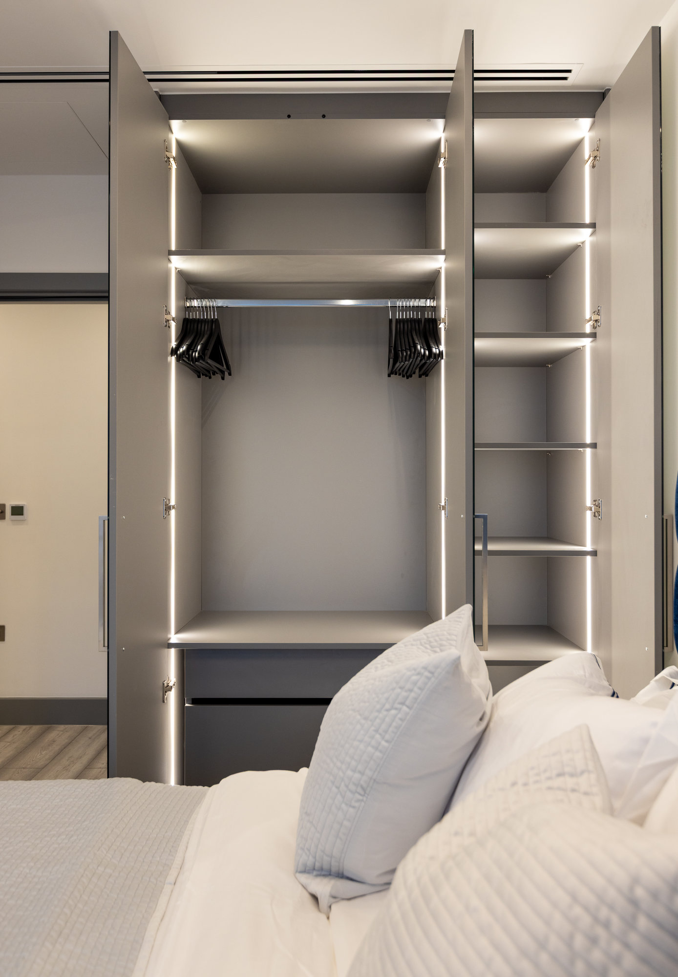 Bespoke fitted wardrobe interior with LED strip lighting, adjustable shelving, and chrome hanging rail in a Kensington apartment bedroom