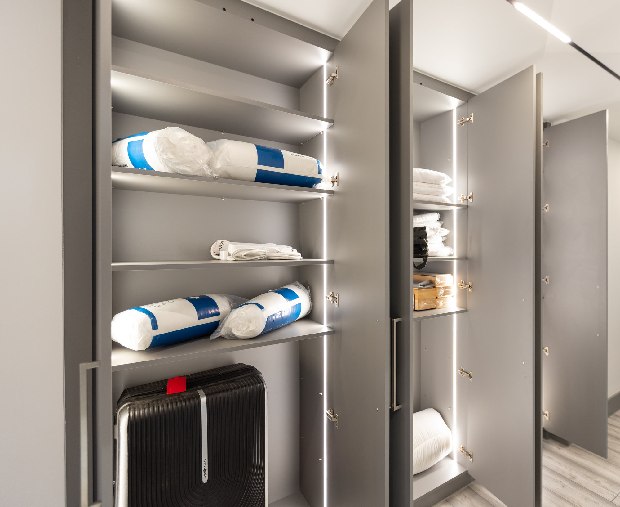 Bespoke fitted wardrobe interior open showing LED-lit shelves storing bedding and luggage in a Kensington utility space