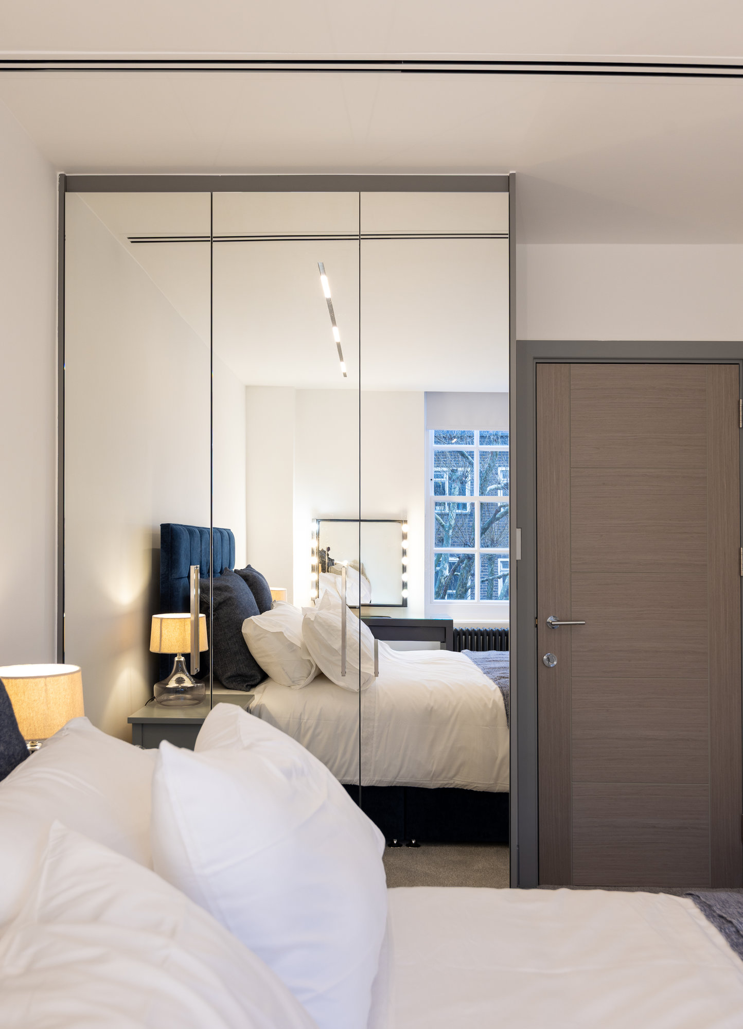 Close-up of bespoke fitted wardrobe with floor-to-ceiling mirrored doors and slim grey frame in a Kensington bedroom