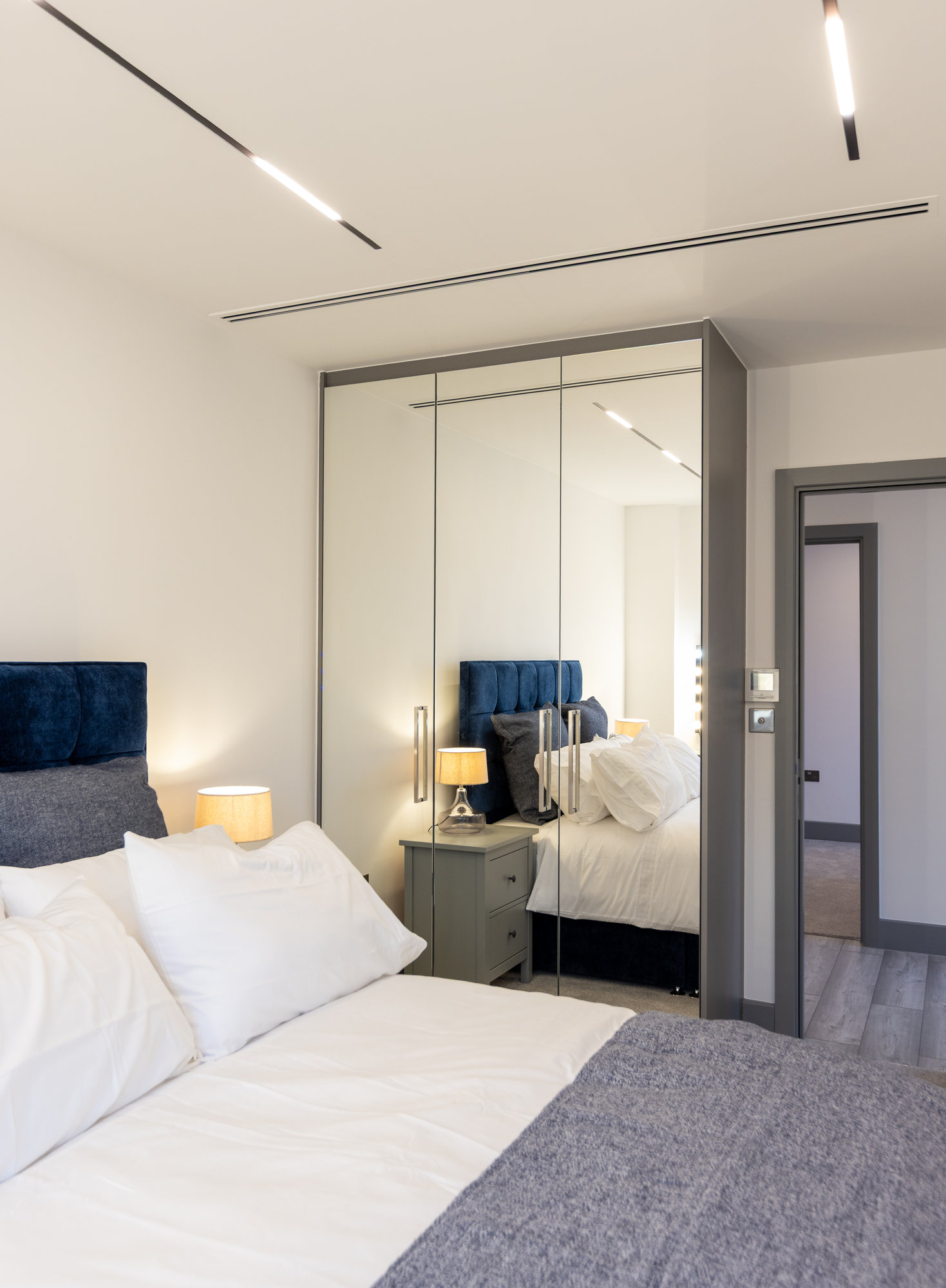 Bespoke fitted wardrobe with mirrored doors and grey frame, side angle view with bedside lamp in a Kensington bedroom