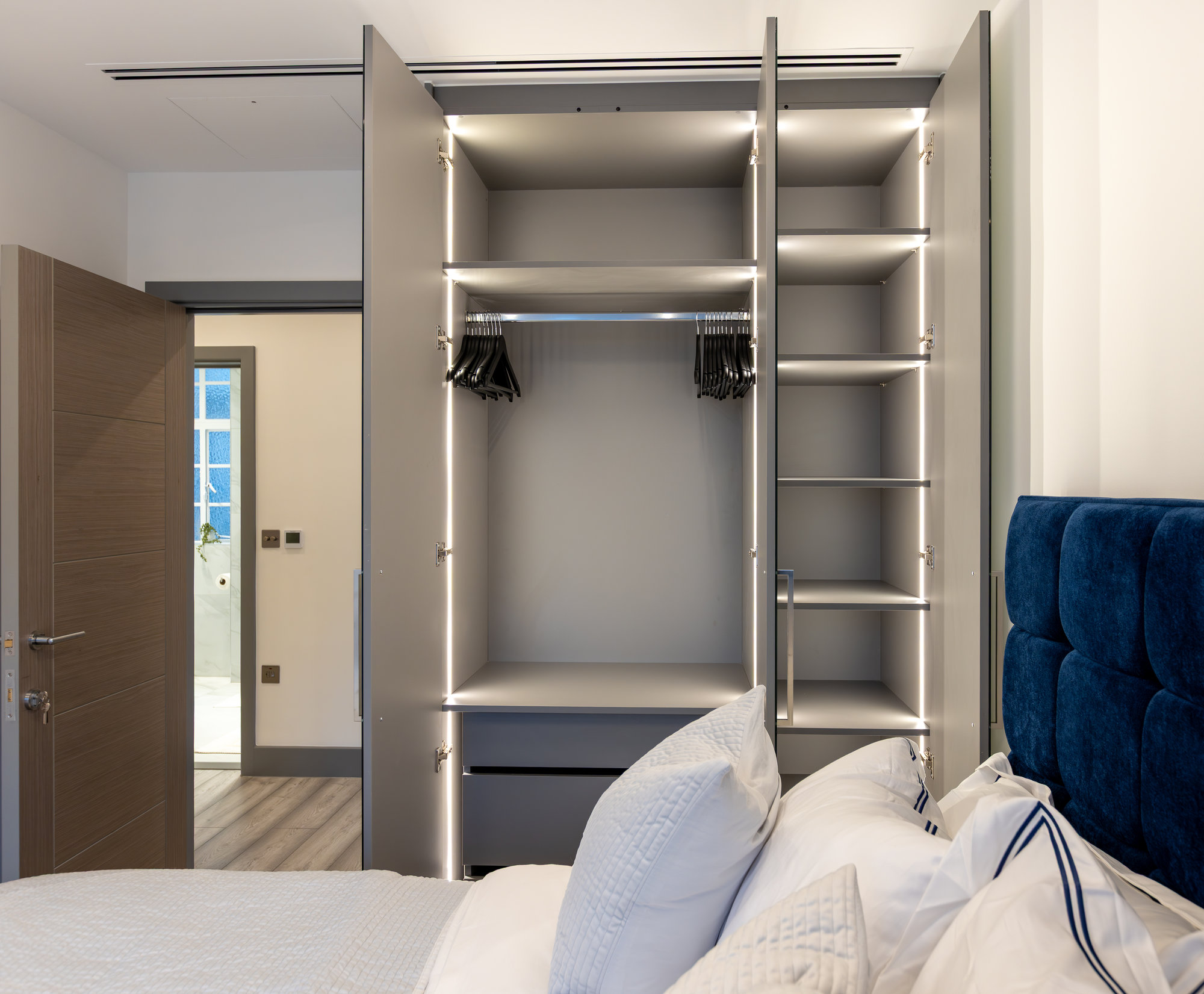 Bespoke fitted wardrobe doors open revealing LED-lit interior with hanging rail and adjustable shelves in a Kensington home