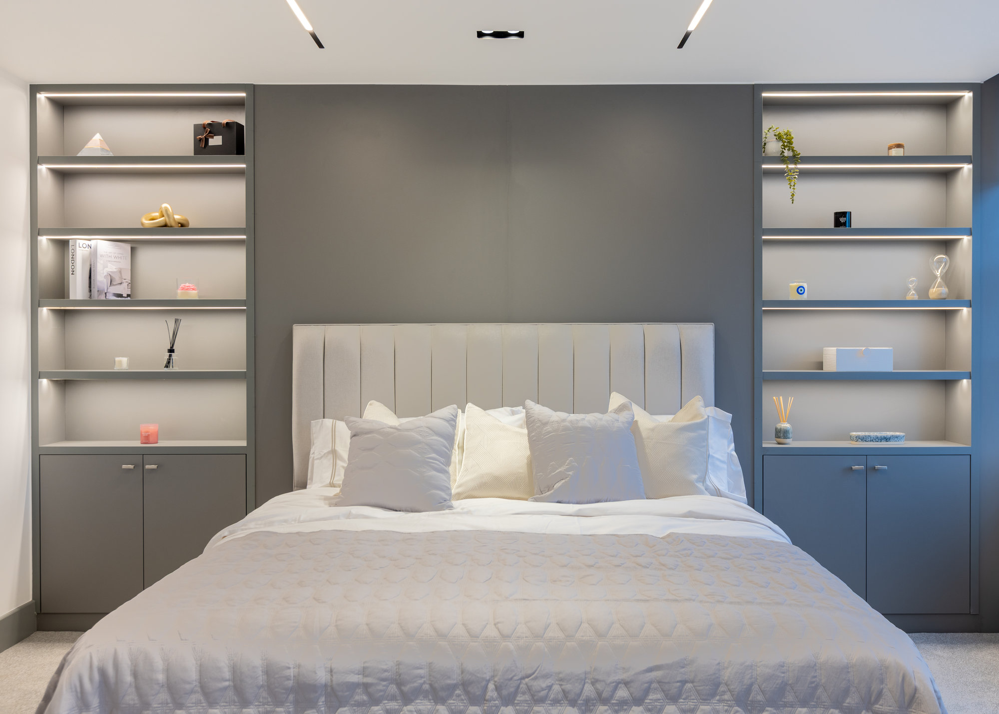 Symmetrical view of a Kensington bedroom with bespoke built-in shelving units flanking an upholstered headboard on a blue-grey feature wall