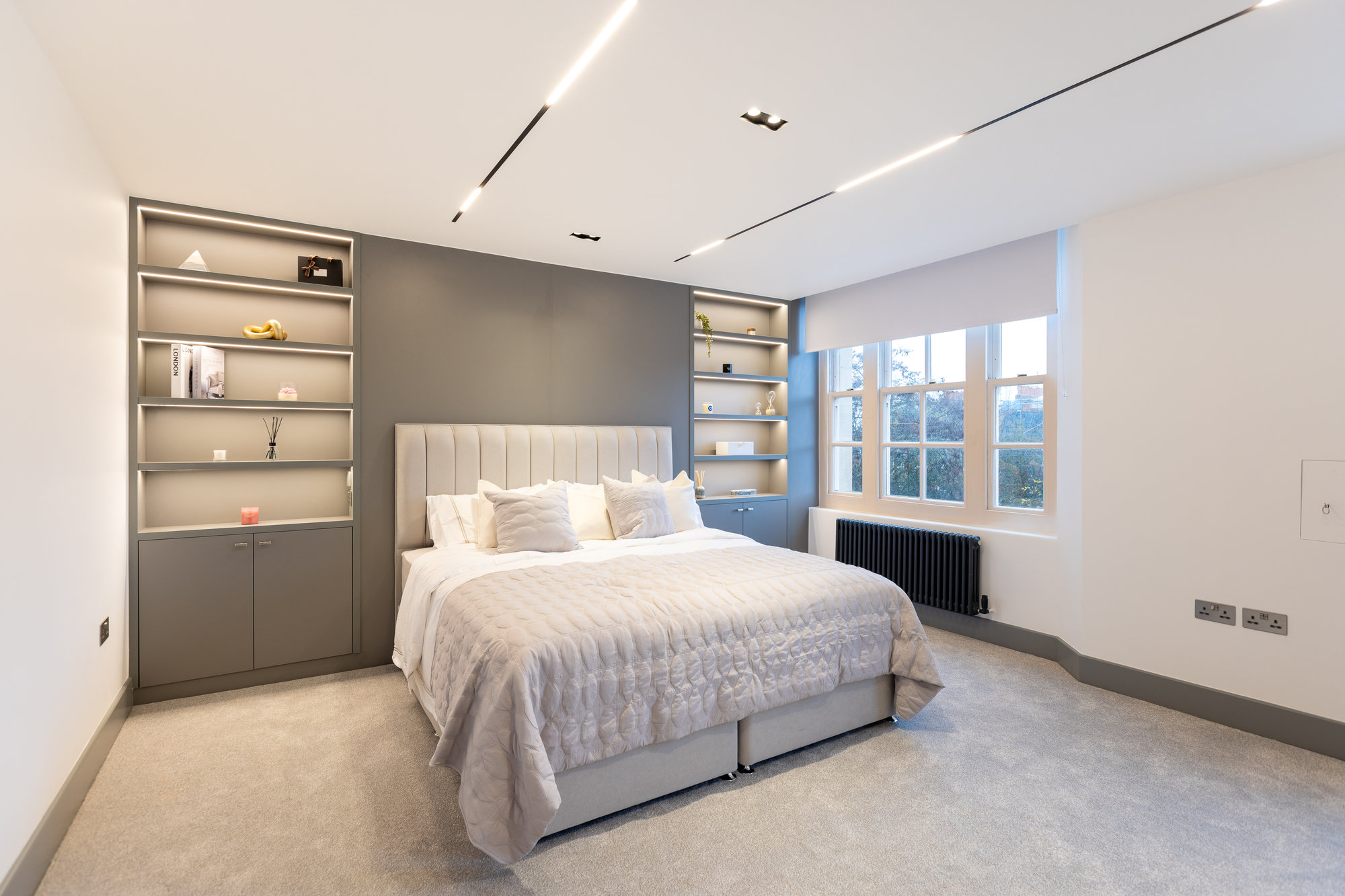 Full room view of a Kensington bedroom featuring bespoke integrated headboard shelving with track lighting on the ceiling