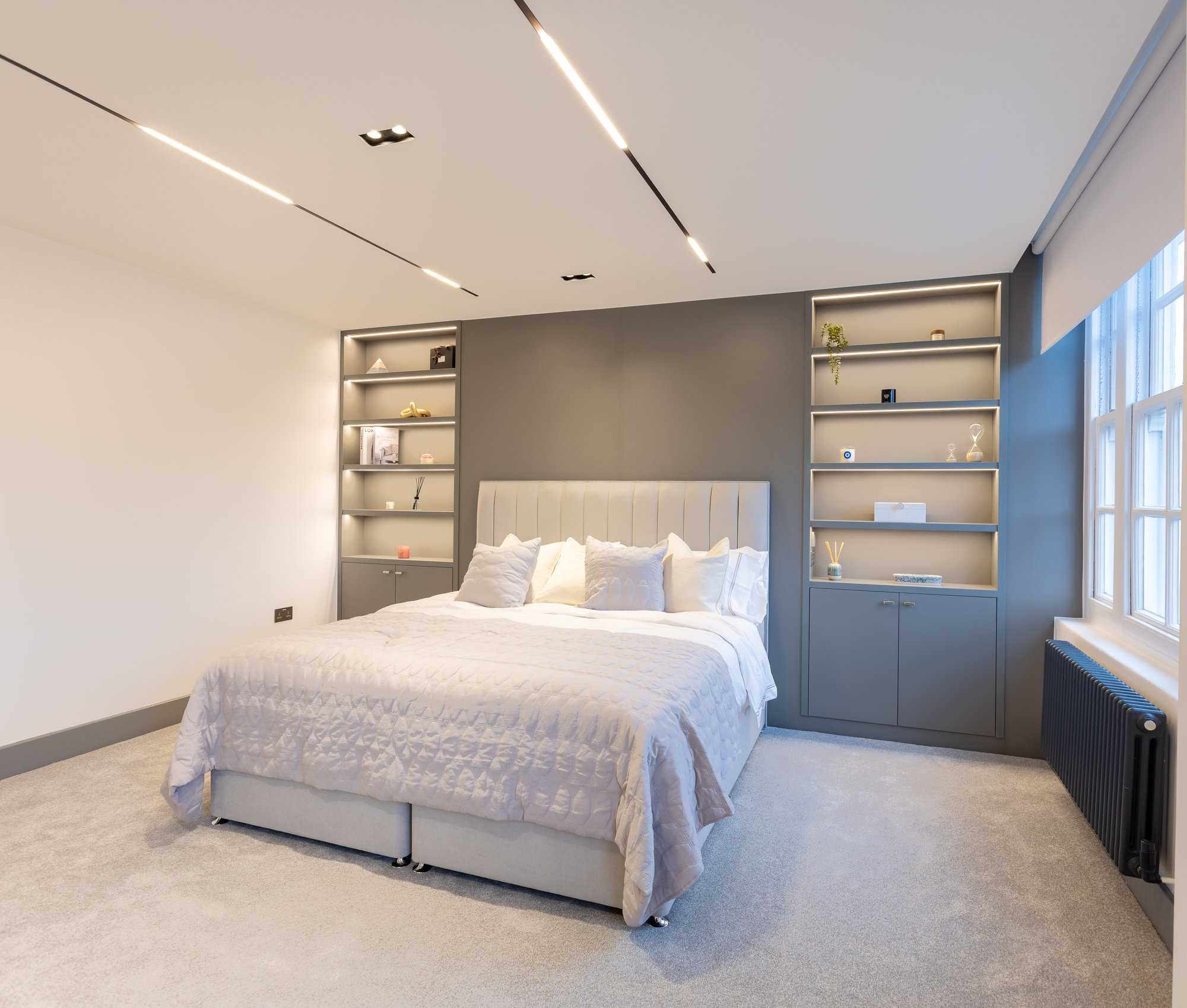 Wide-angle view of a modern Kensington bedroom with matching bespoke shelving units on both sides of the headboard wall