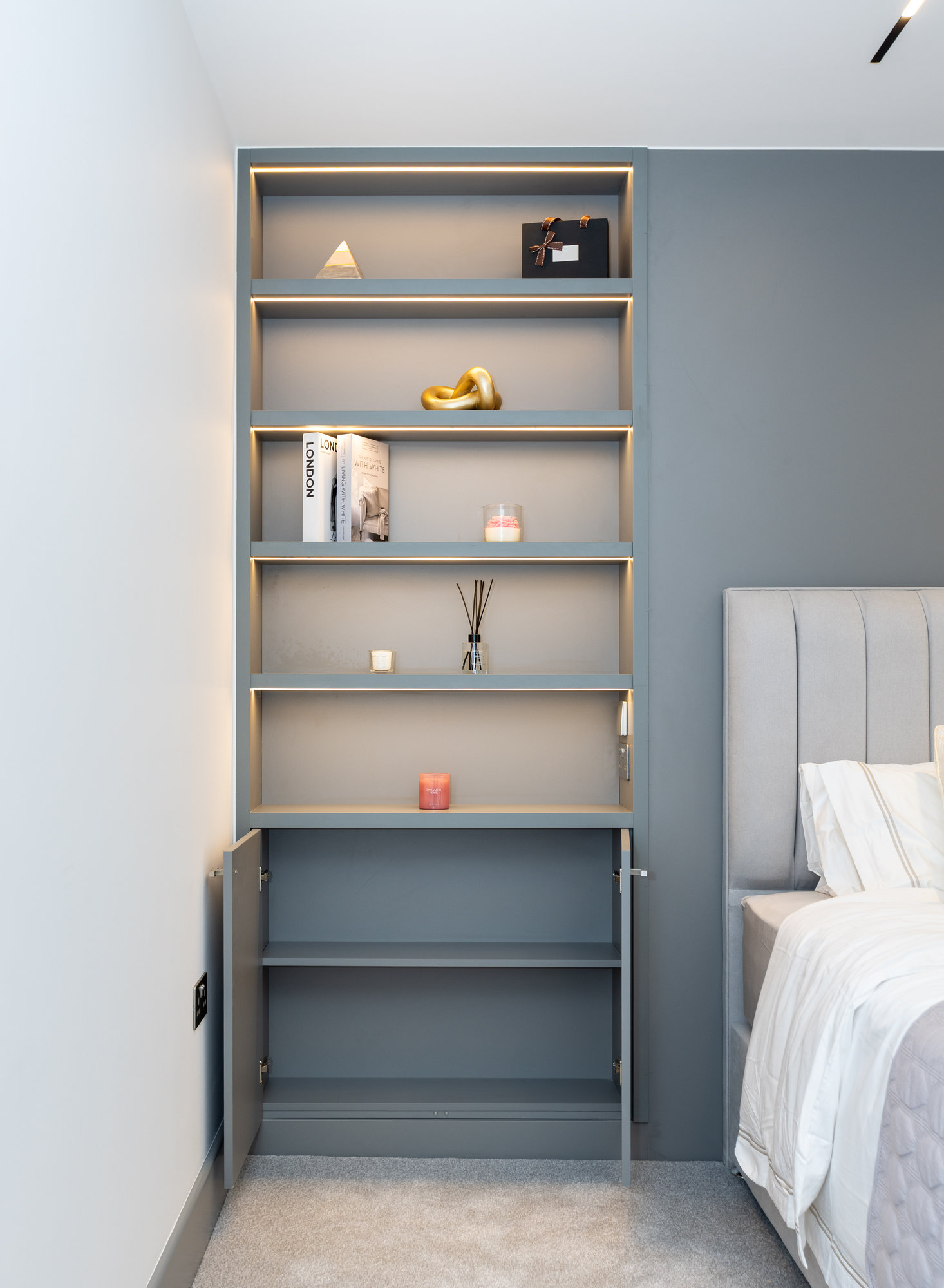 Detail view of bespoke headboard shelving unit with cupboard doors open showing interior storage in a Kensington bedroom
