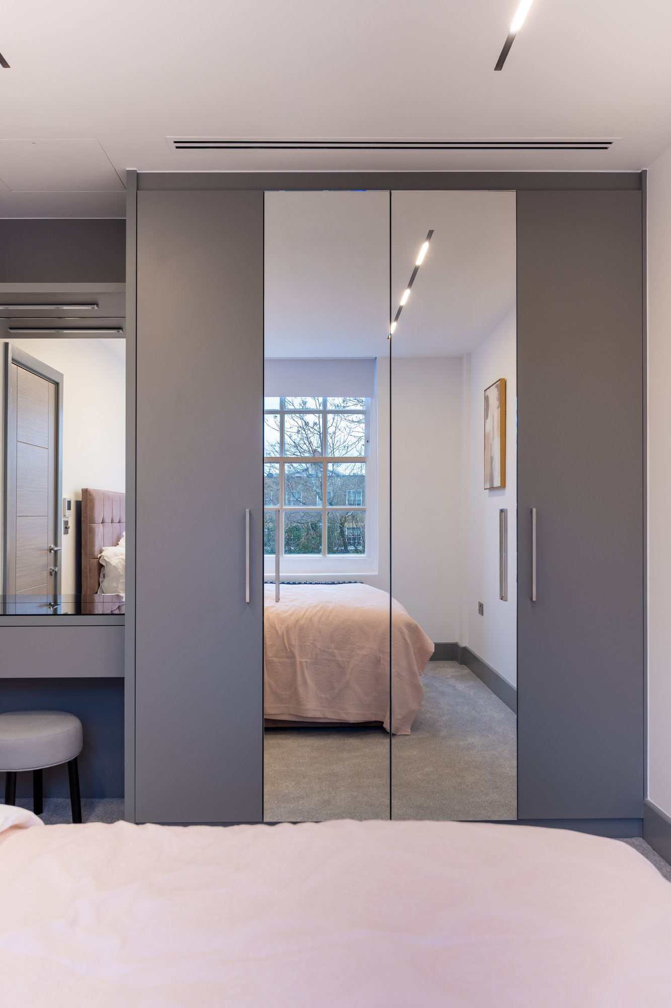 Bespoke grey wardrobe with mirrored doors and integrated vanity desk with upholstered stool in a Kensington bedroom
