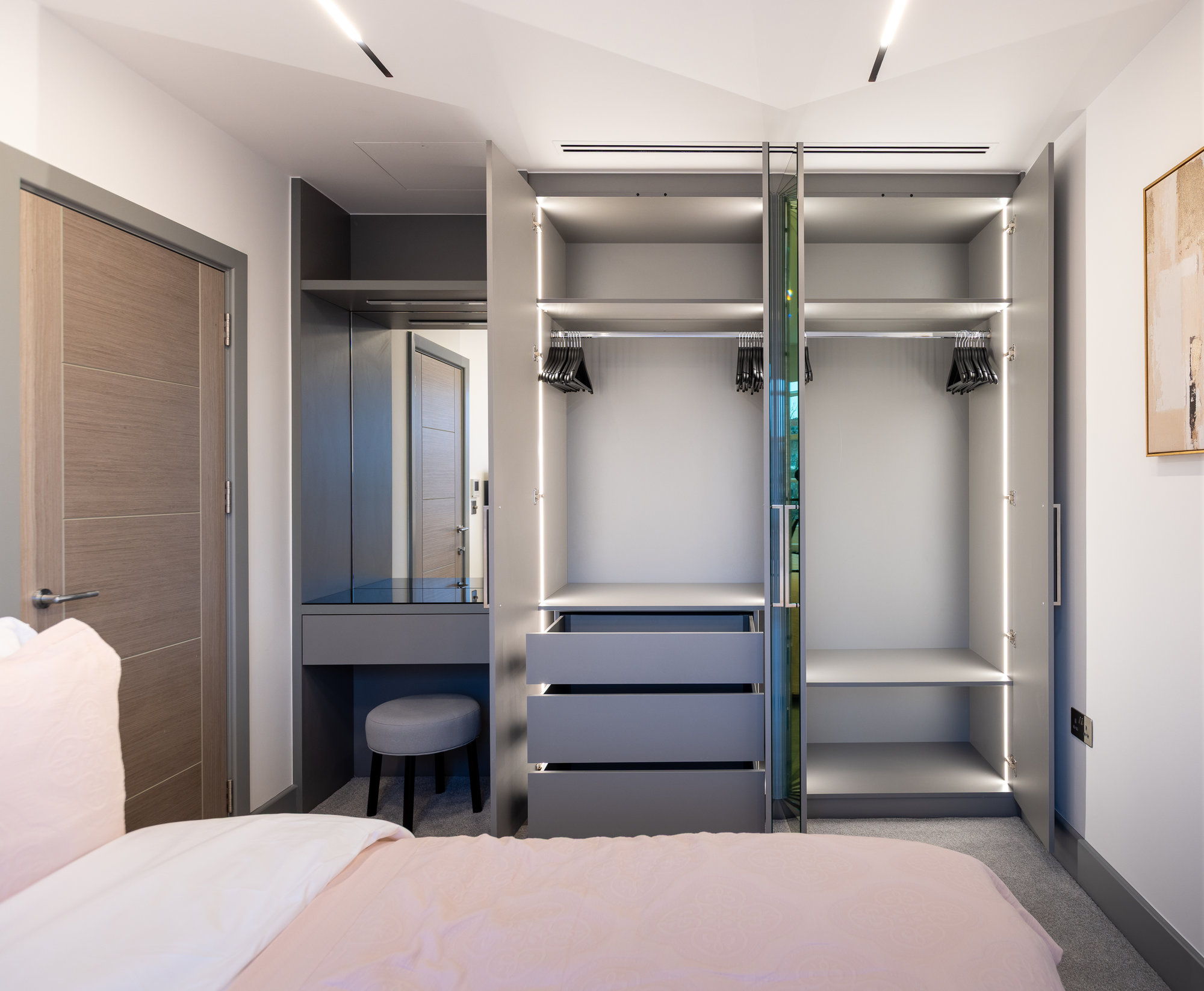 Bespoke fitted wardrobe with central mirrored doors closed and integrated vanity desk to the left in a Kensington bedroom