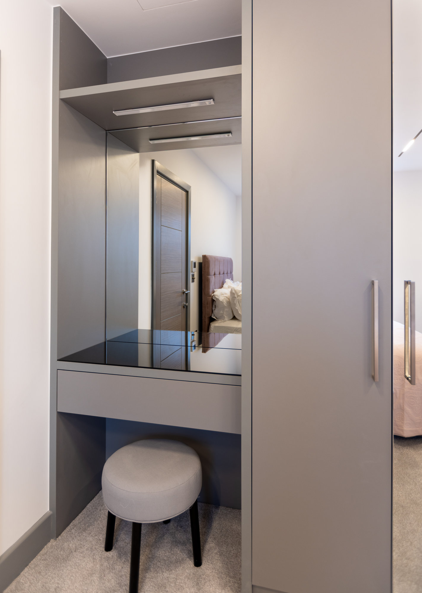 Built-in bespoke vanity nook with glass-top desk, integrated mirror, and padded stool adjacent to a fitted wardrobe in Kensington