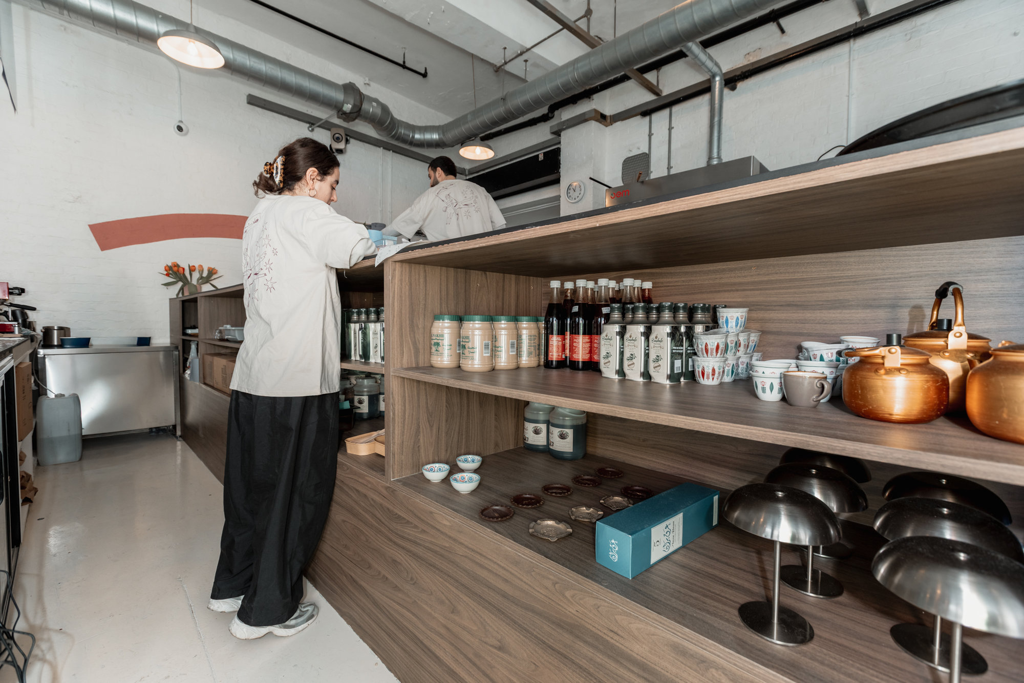 Bespoke walnut back-bar shelving displaying tea canisters, copper kettles, and ceramics behind the service counter in Dalston