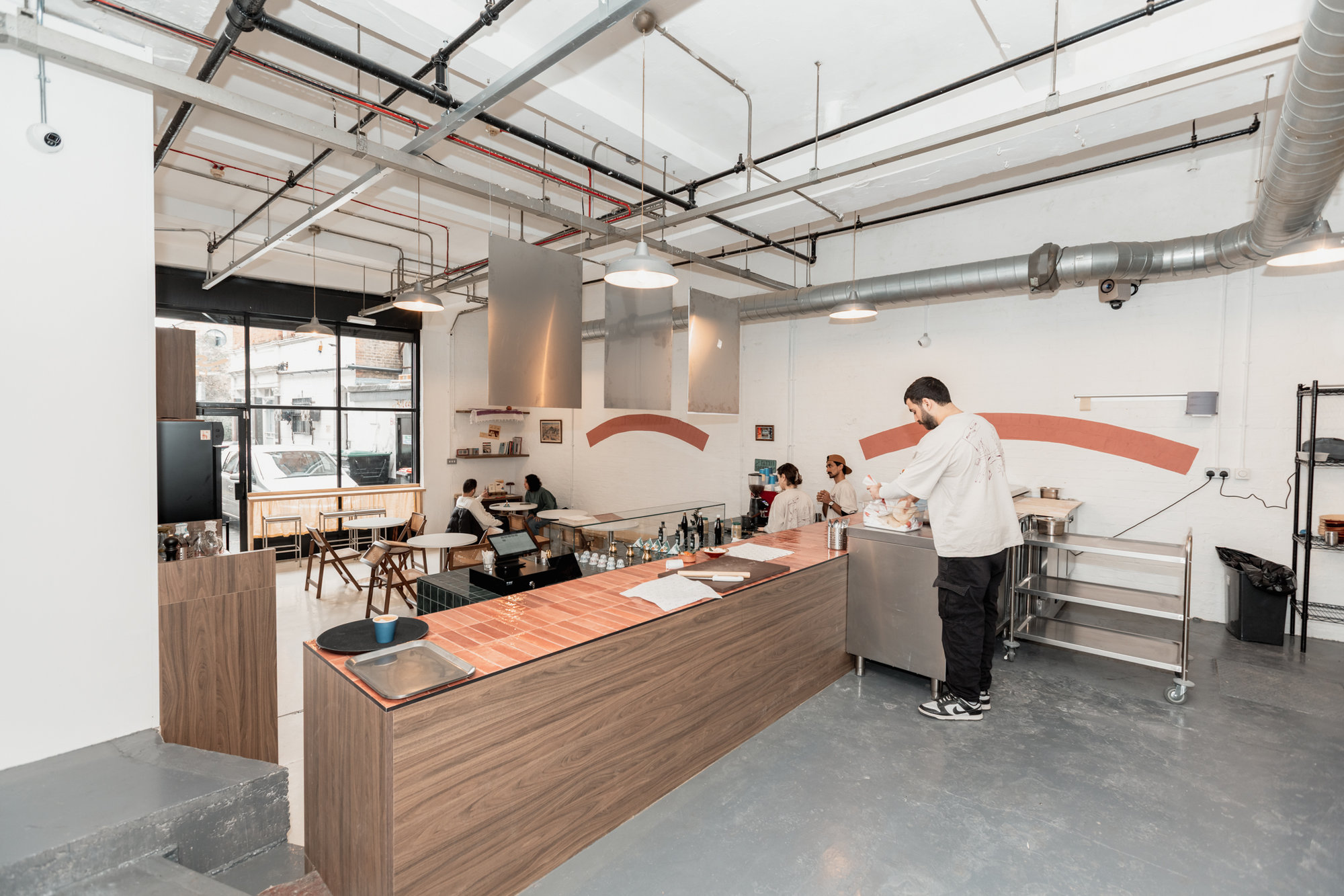 Bespoke walnut service counter with copper-top surface and open kitchen behind in a contemporary Dalston restaurant