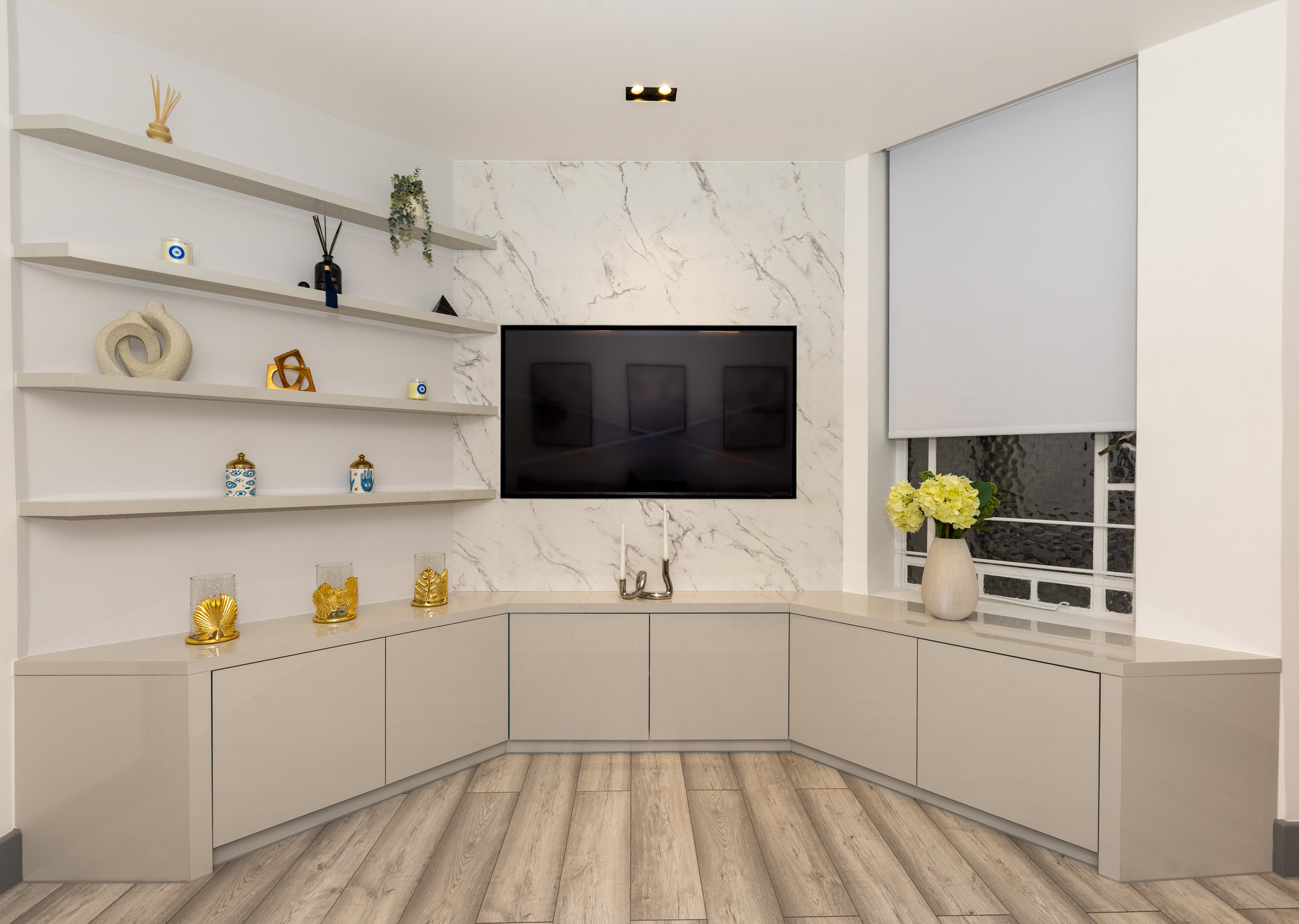 Bespoke corner TV media wall with marble-effect back panel, wall-mounted screen, floating display shelves, and low-level cupboards in a Kensington living room