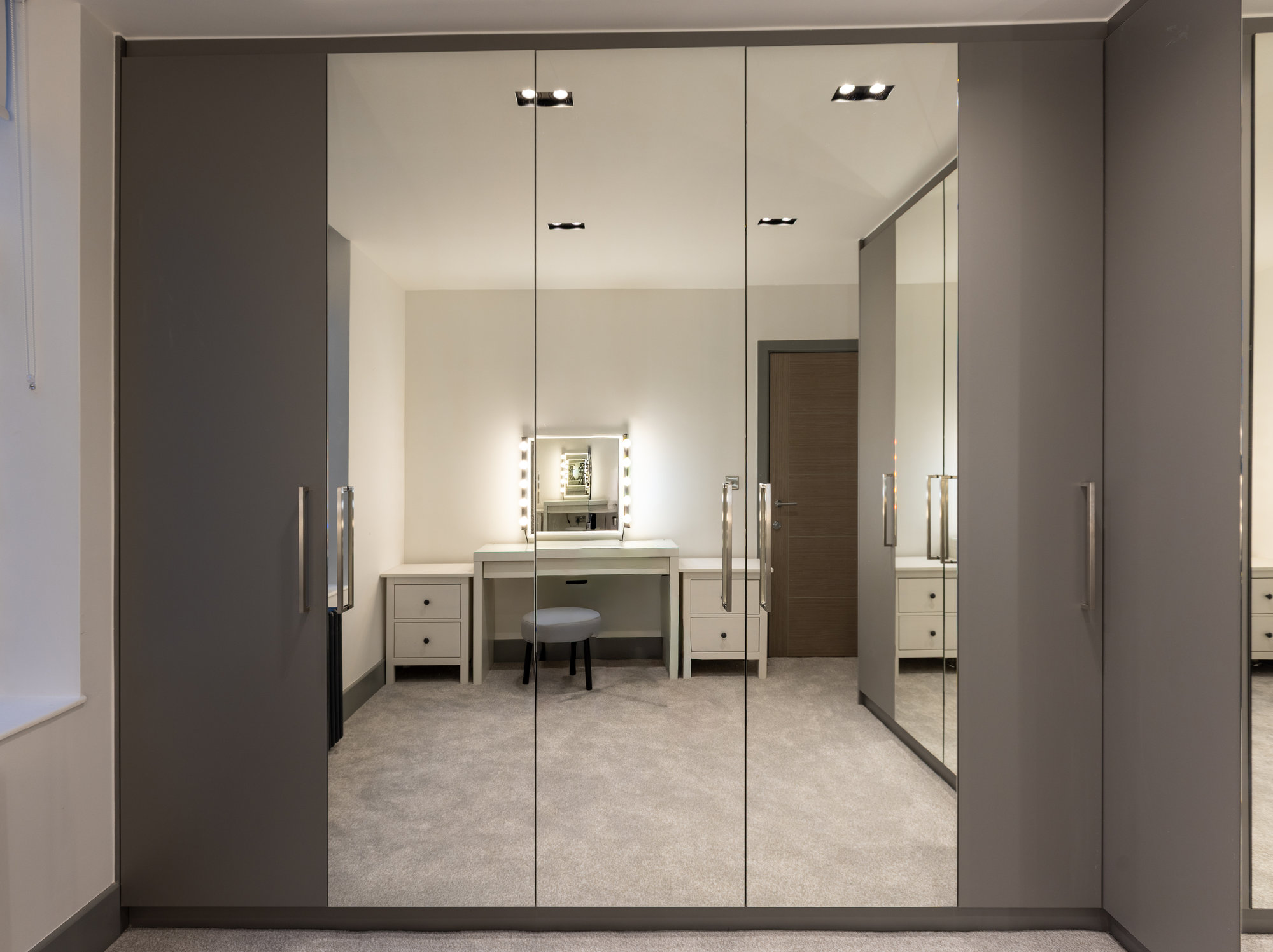 Floor-to-ceiling bespoke mirrored walk-in wardrobe doors reflecting a Hollywood-style vanity mirror and stool in Kensington