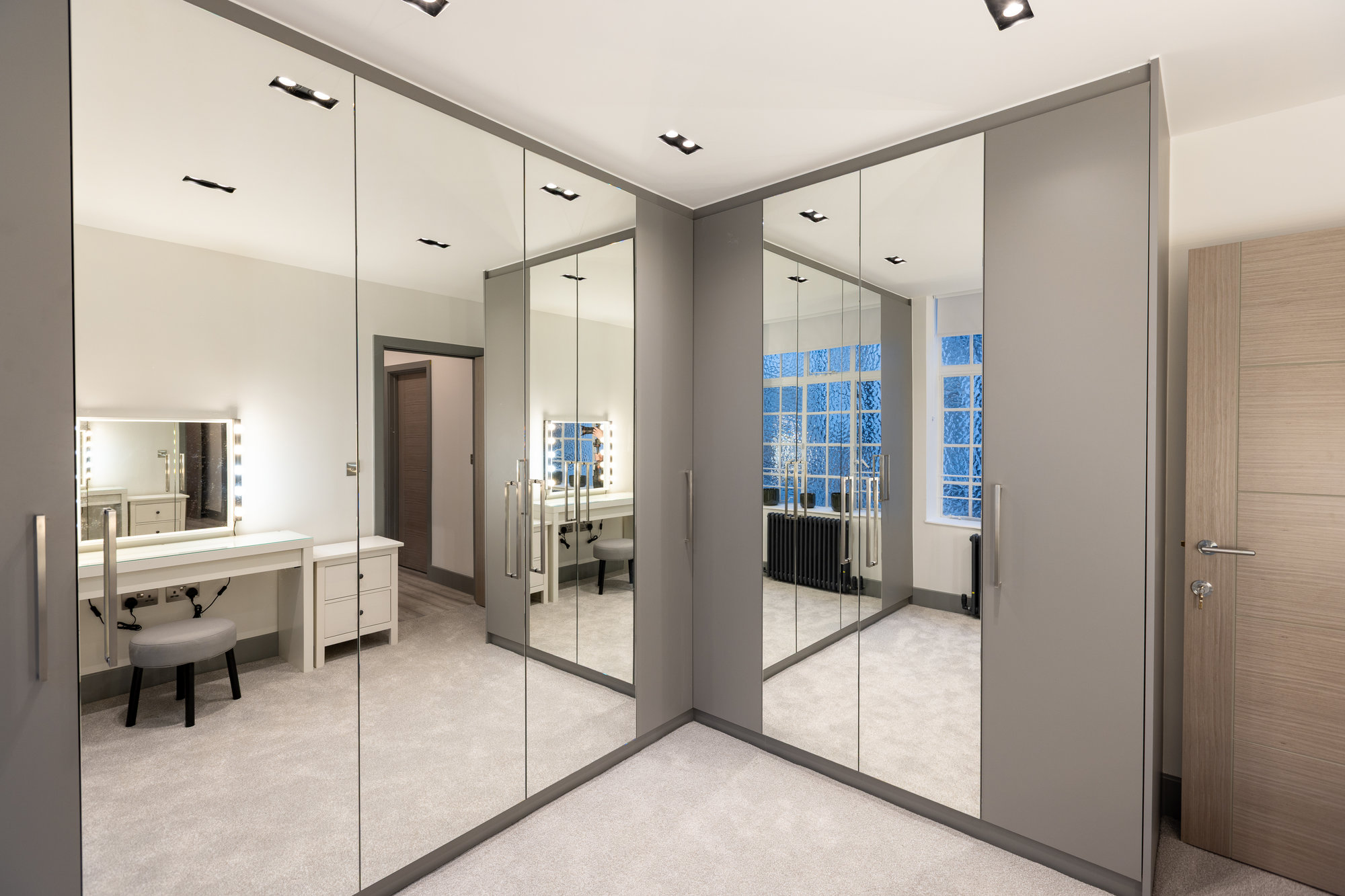 L-shaped bespoke walk-in wardrobe with floor-to-ceiling mirrored doors and vanity table reflected in a Kensington dressing room