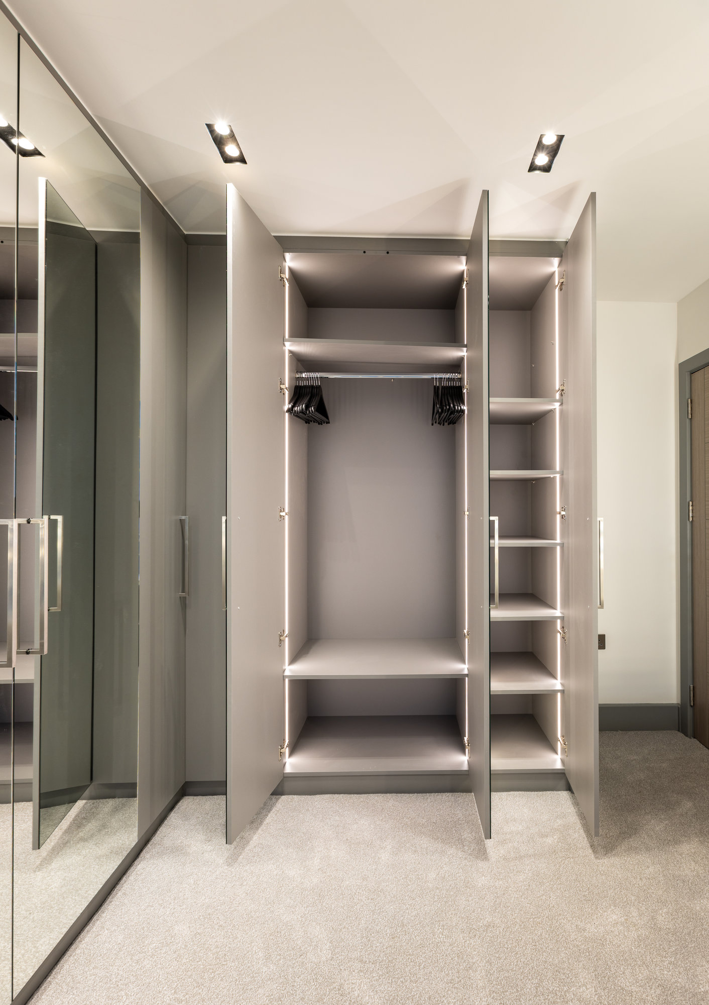 Bespoke walk-in wardrobe open revealing LED-lit interior with shelving, dual hanging rails, and adjustable compartments in Kensington