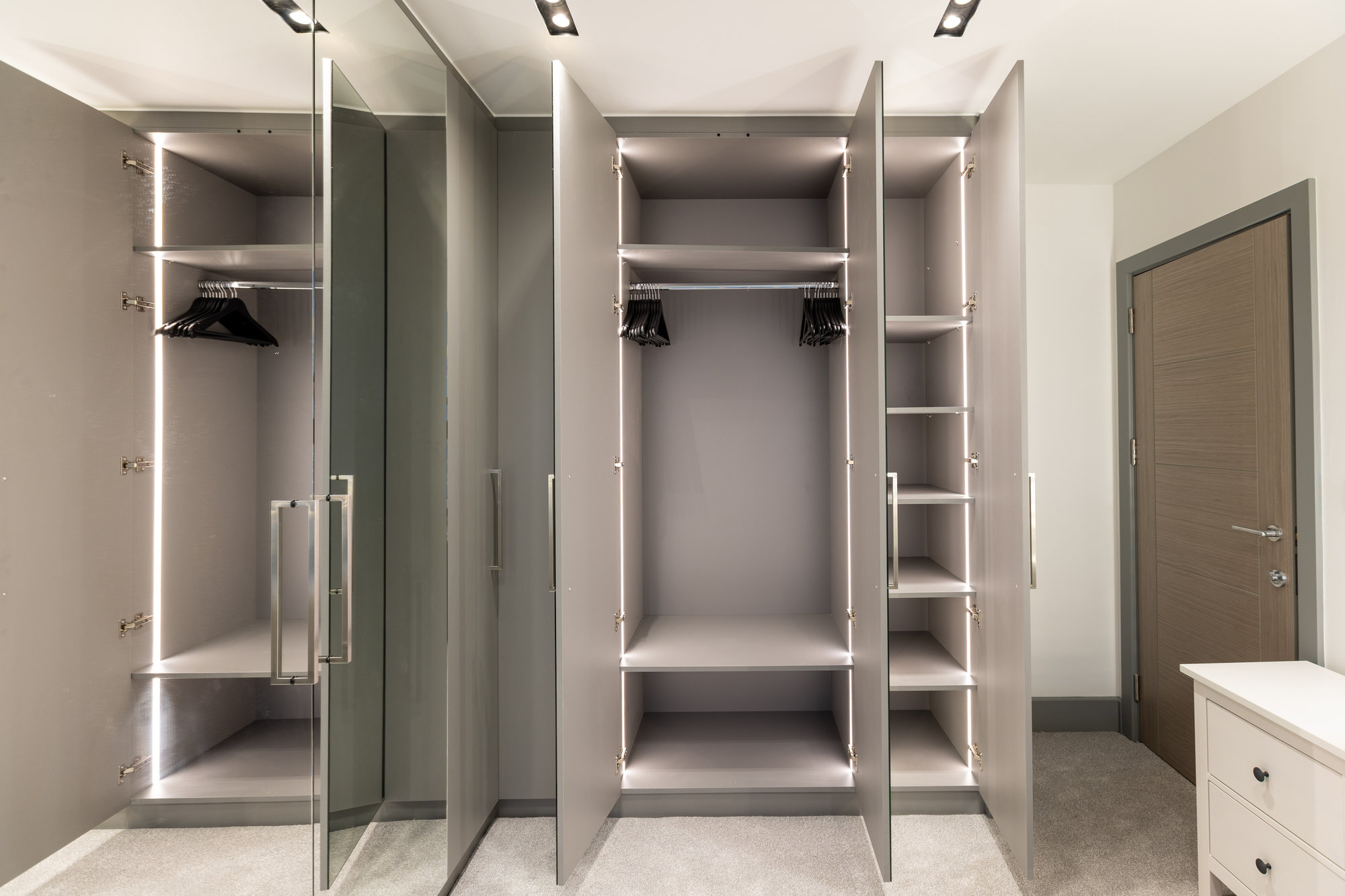 Bespoke walk-in wardrobe doors open showing interior with adjustable shelves, hanging rails, and shoe storage in Kensington