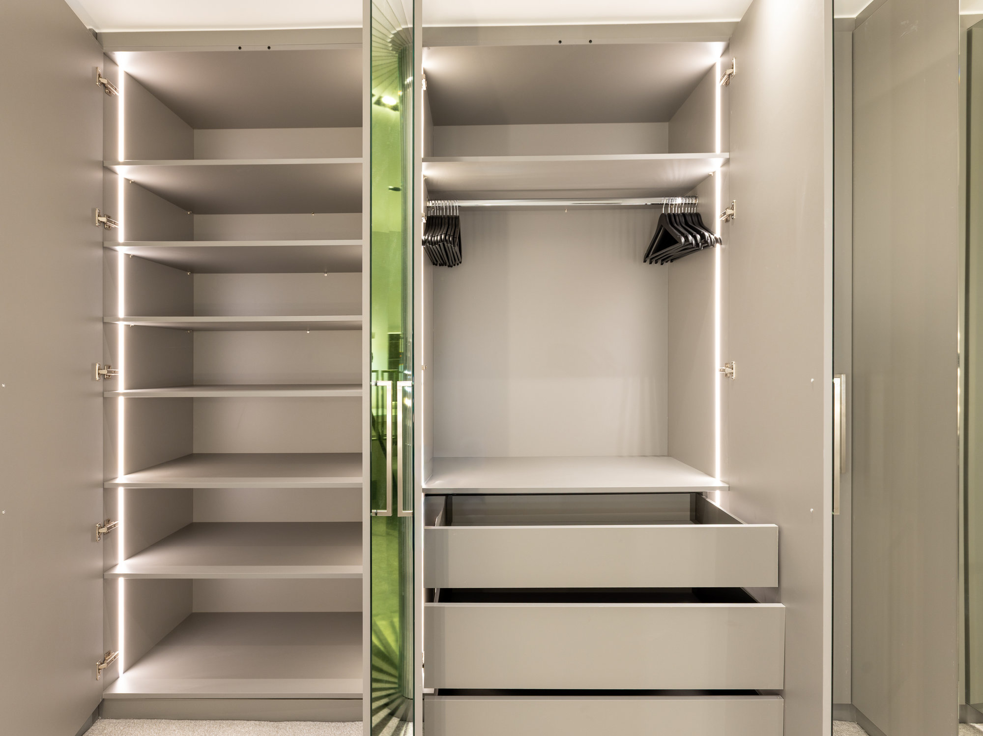 Bespoke walk-in wardrobe interior with LED-lit adjustable shelves, pull-out drawers, and hanging rails in a Kensington dressing room