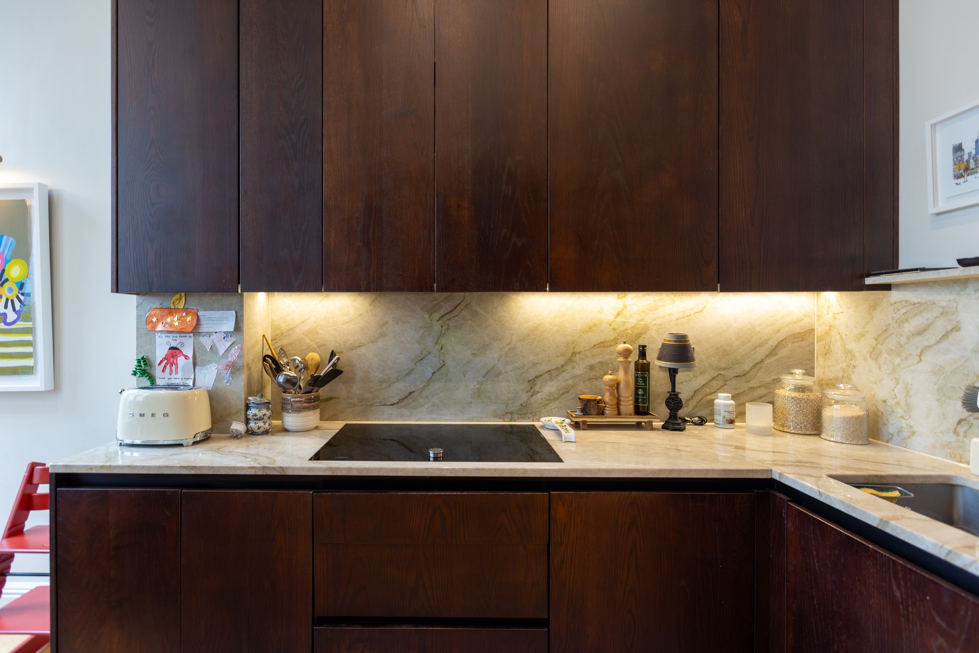 Bespoke dark oak kitchen with induction hob, marble worktop and splashback, and warm under-cabinet LED lighting in a Kensington home