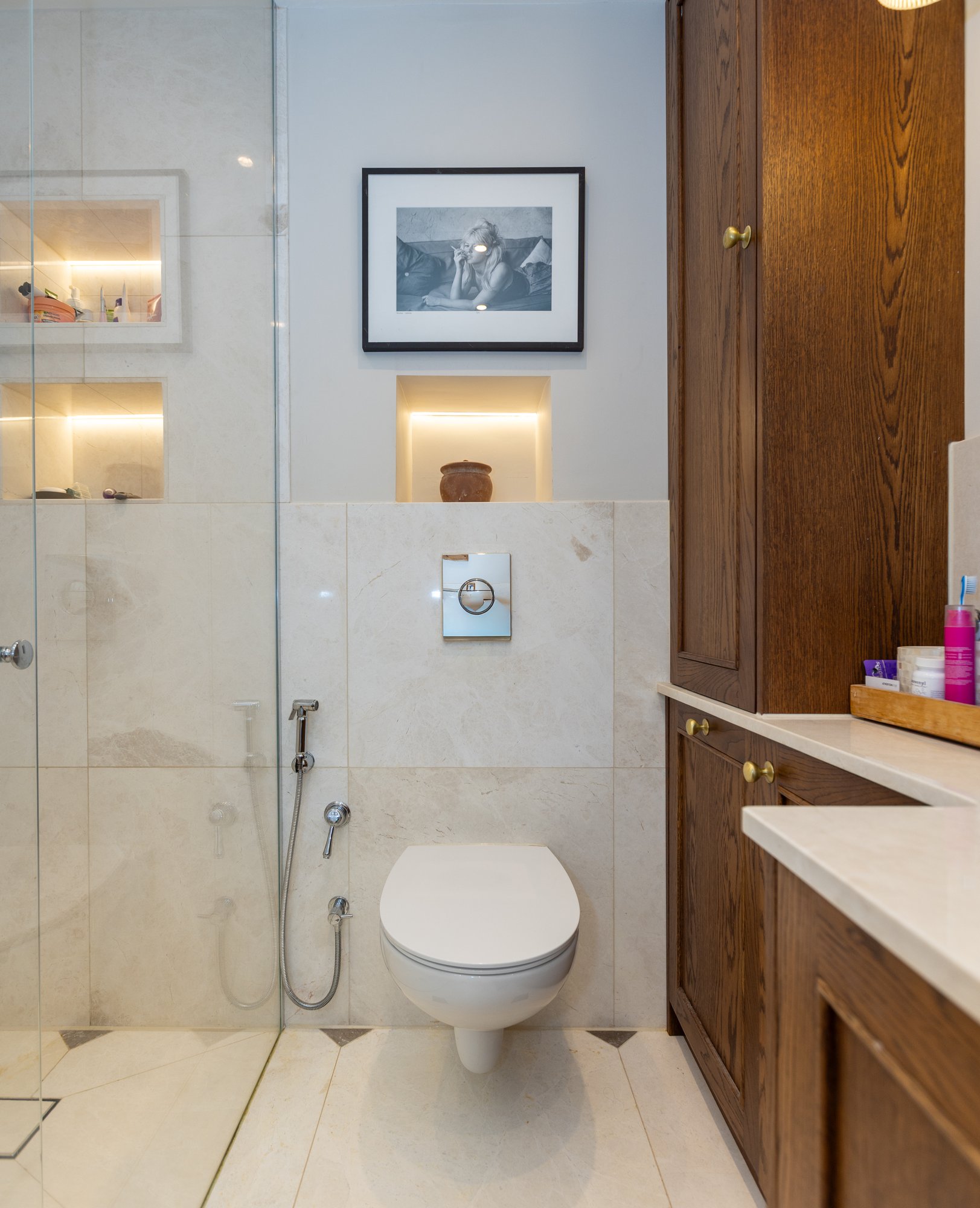 Bespoke dark oak fitted bathroom cabinet with brass knob handles beside a walk-in shower enclosure and wall-hung toilet in a Kensington bathroom