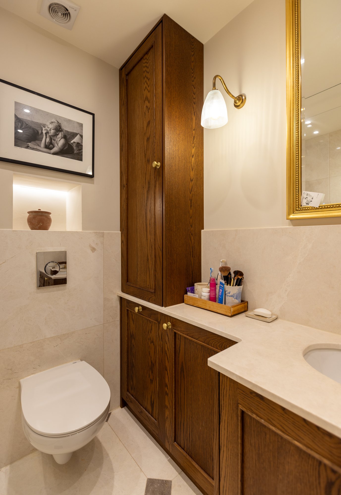 Bespoke dark oak bathroom storage tower and vanity unit with marble worktop and brass wall sconce in a Kensington bathroom