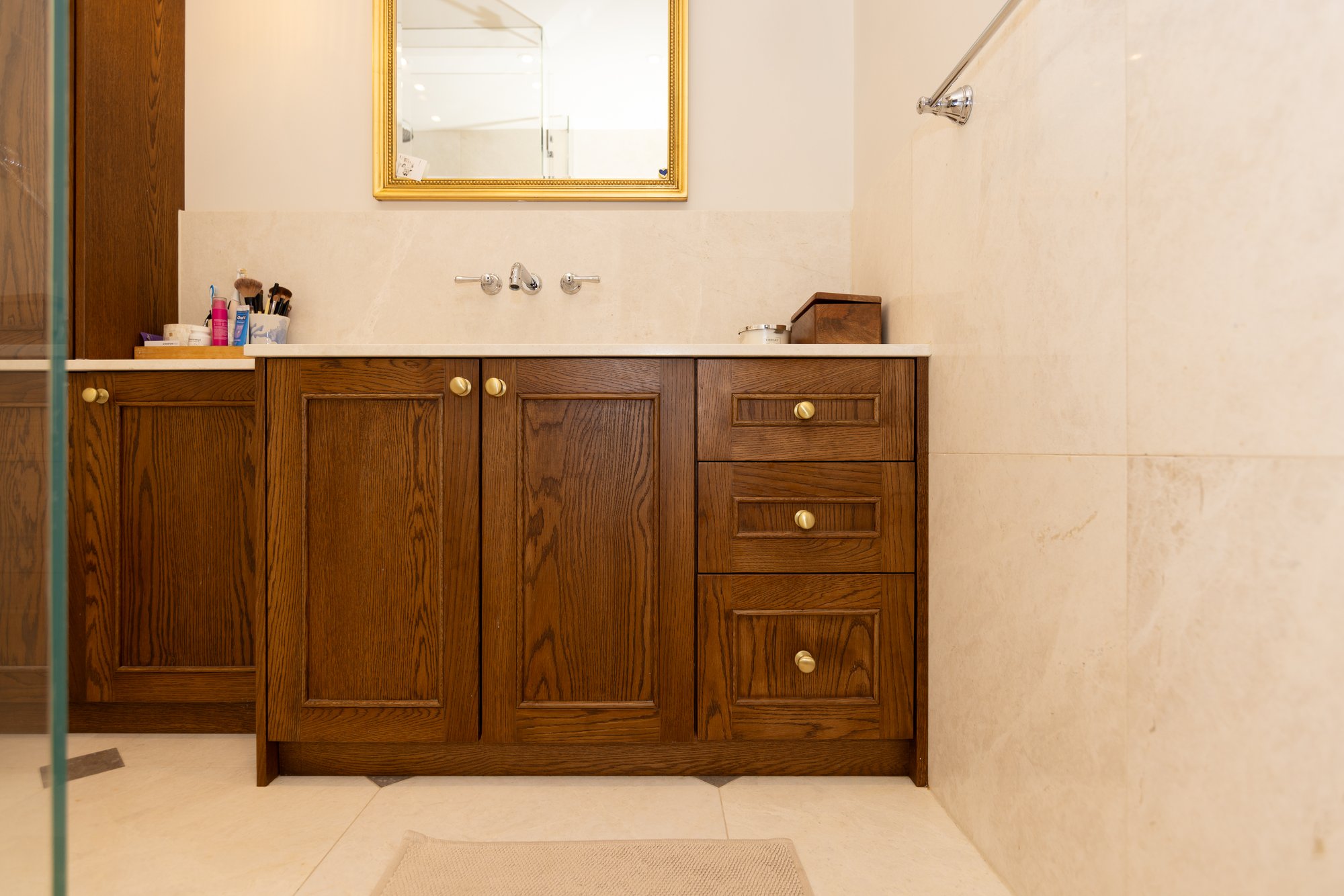 Close-up of bespoke dark oak bathroom vanity cabinet with panel doors, three drawers, brass knob handles, and marble worktop in a Kensington bathroom