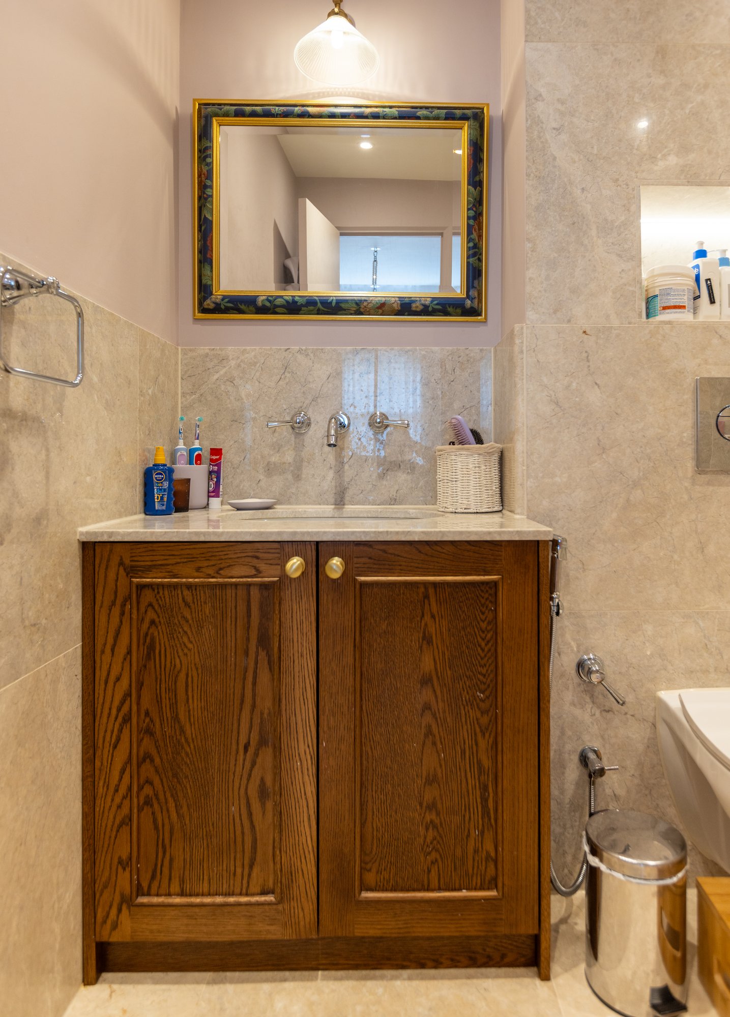 Bespoke dark oak two-door bathroom vanity unit with brass knobs, marble splashback, and decorative framed mirror in a Kensington en-suite